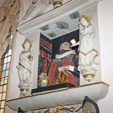 Wall monument: bearded man with mathematical instruments surrounded by allegorical figures. Viewed from right.