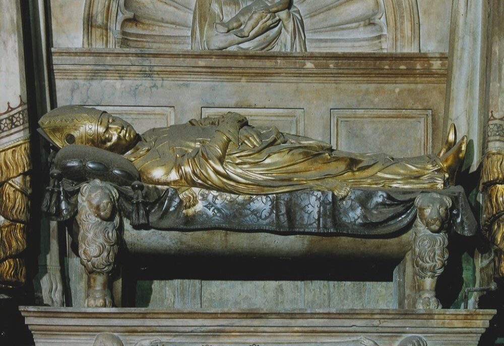 Wall monument with effigy of mitred bishop on couch with lion feet. Above the Virgin and Child in shell tympanum. Inscription plaque below.
