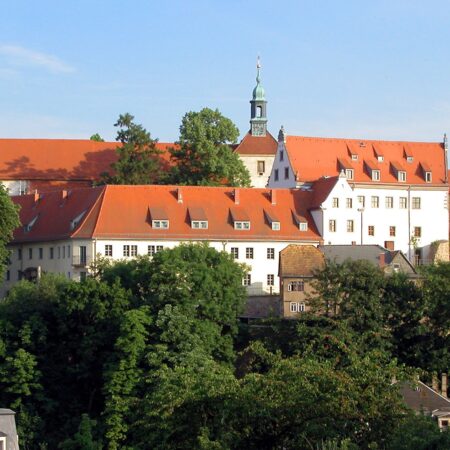 . The Afraberg today with a view of the Afrakirche, Meissen (Saxony, Germany). . White building with red roofs, surrounded by trees.