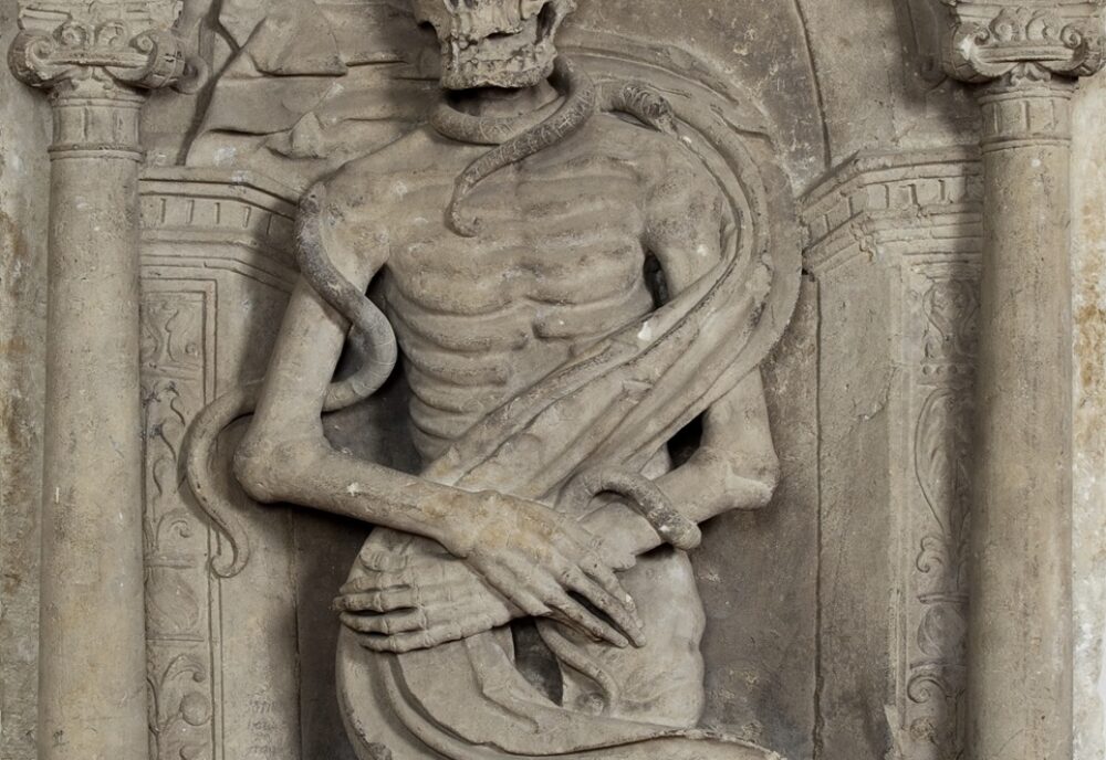 Upper body of cadaver effigy showing shroud and snakes
