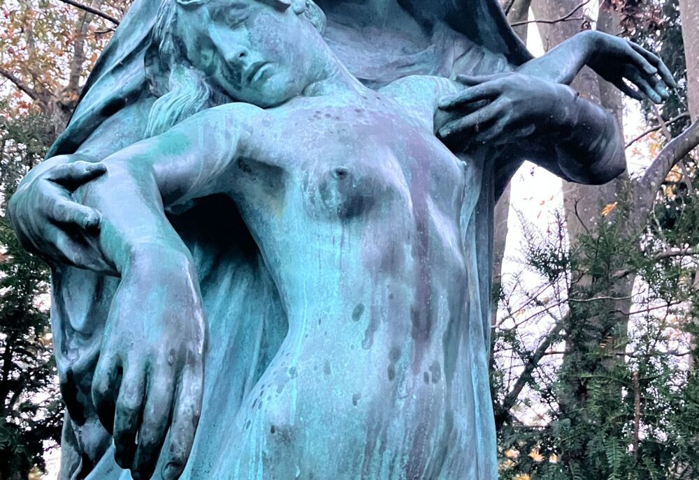 Sculpture of a hooded figure supporting the body of a young woman, naked apart from very thin drapery