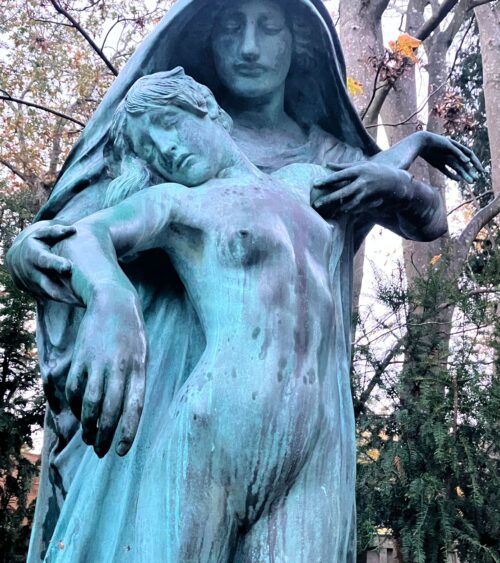 Sculpture of a hooded figure supporting the body of a young woman, naked apart from very thin drapery