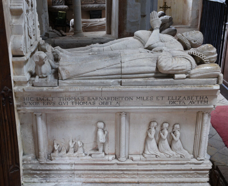 Chest tomb with effigies of male and female in late C16 dress. Kneeling children on side of chest.