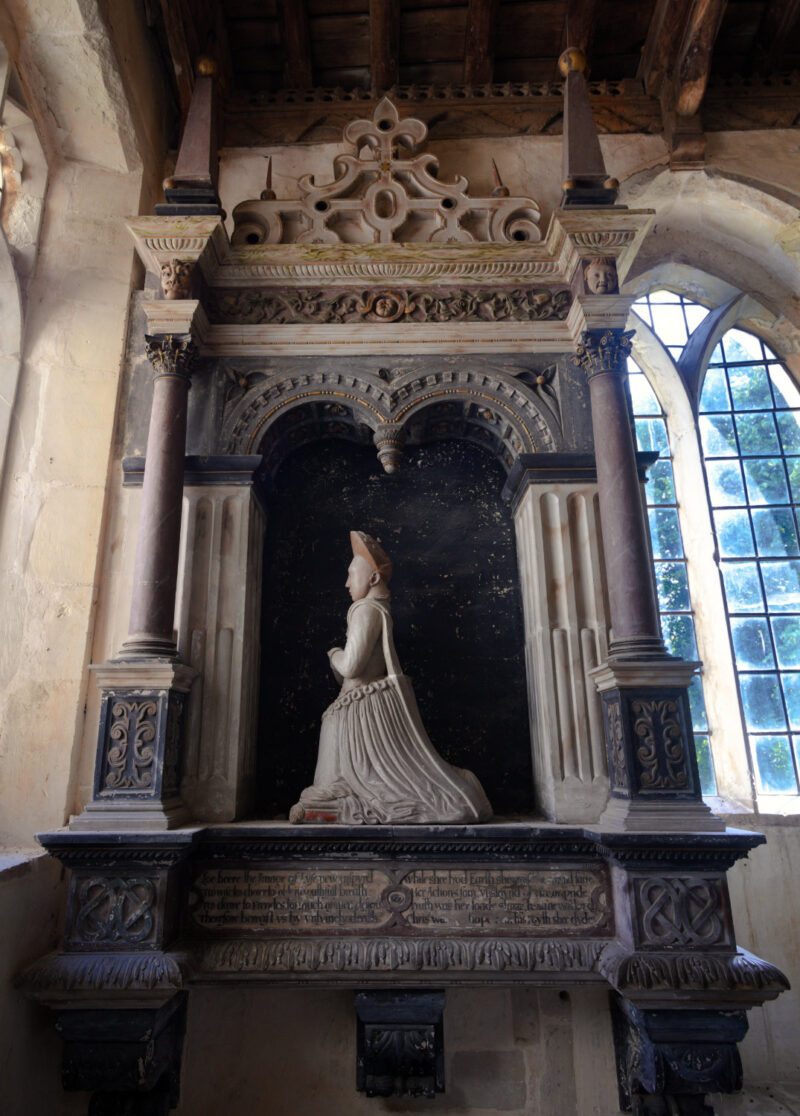 Wall monument with kneeling effigy of young woman, hands clasped in prayer