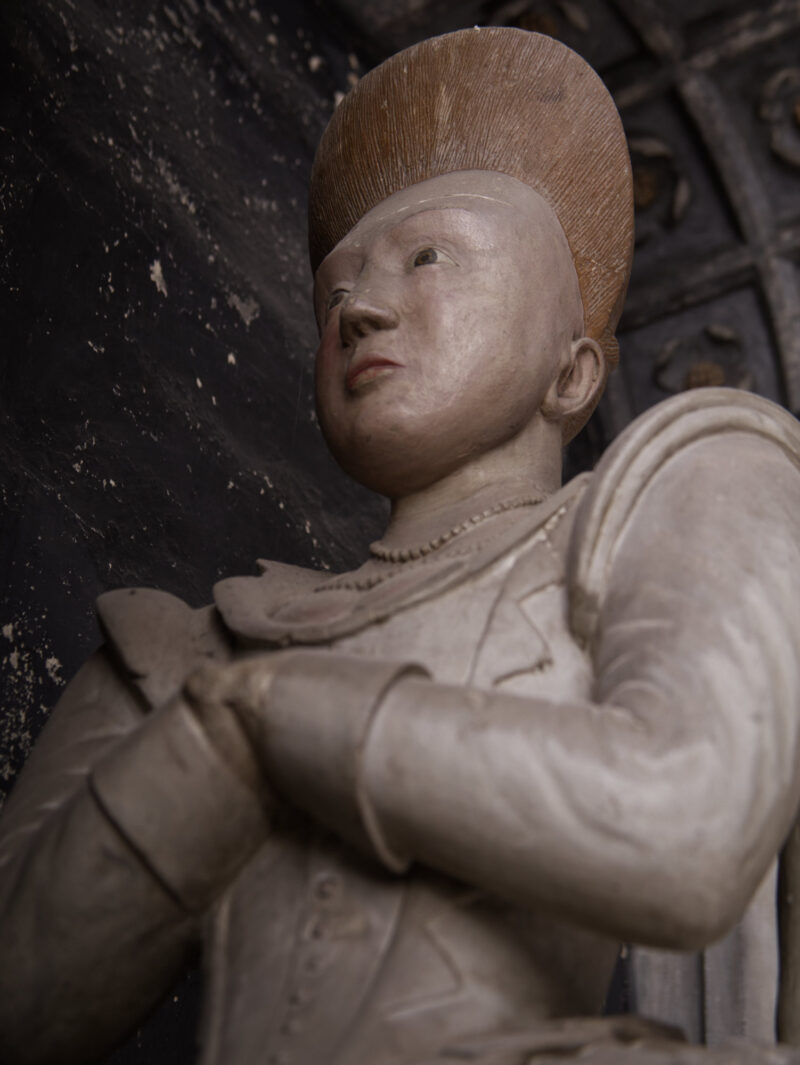 Detail of effigy of young woman, kneeling, with elaborate hair style