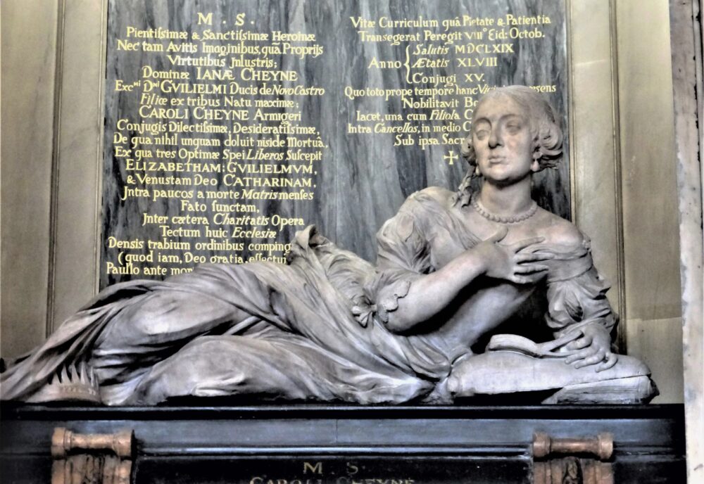 Effigy of woman in late C17 dress, reclining on plinth and reading a book