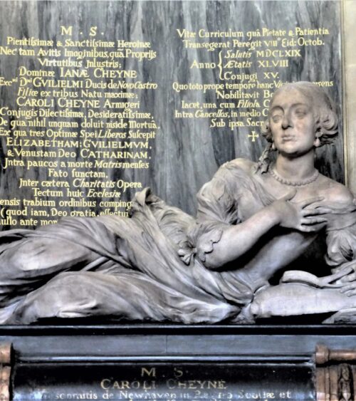 Effigy of woman in late C17 dress, reclining on plinth and reading a book