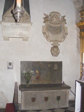 Monumental brass set in wall above tomb chest.
